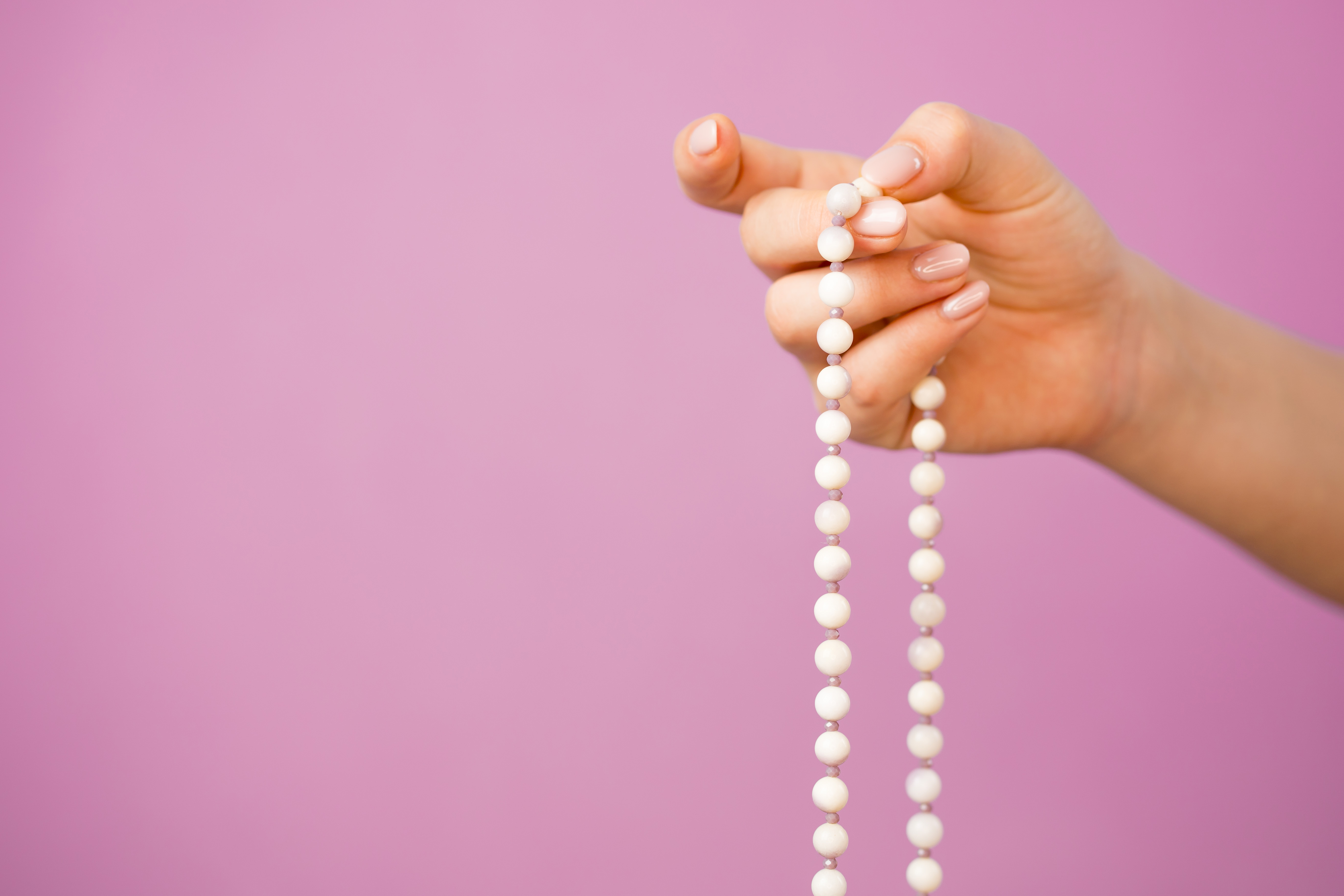 Woman, lit hand close up, counts Malas, strands of gemstones beads used for keeping count during mantra meditations on pink background
